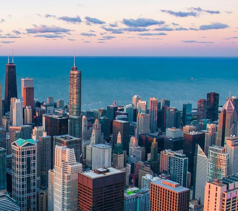 starting a business in Dubai - Aerial view of a dense cityscape with skyscrapers near a large body of water at dusk. 