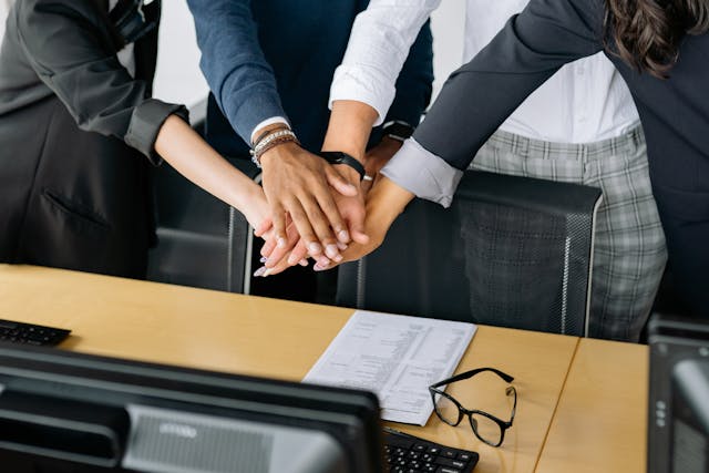  starting a business in Dubai - Team members stacking hands over a table in a show of unity with documents and glasses nearby.