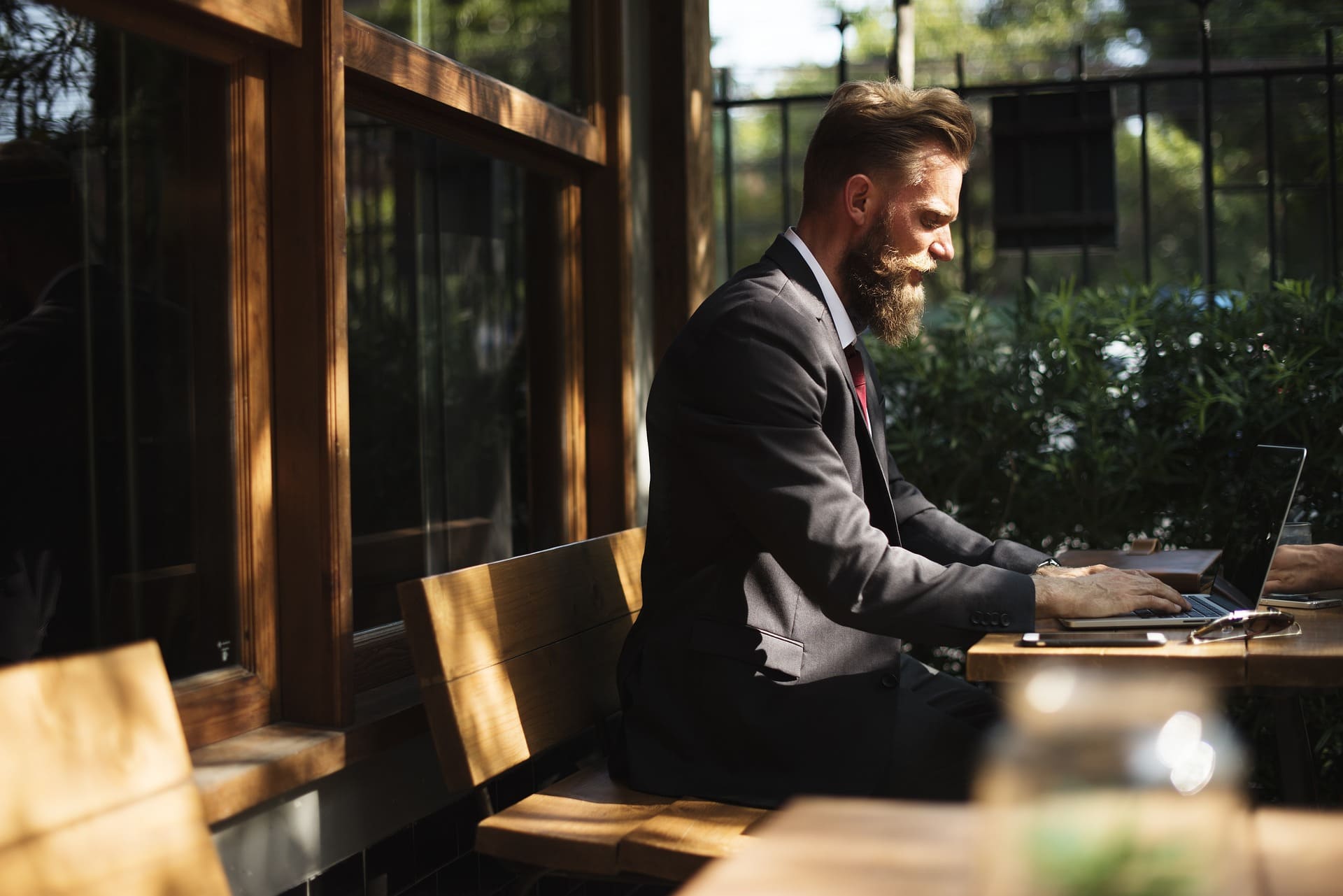 Business Setup from the UK - Man in a suit working on a laptop at an outdoor cafe table.