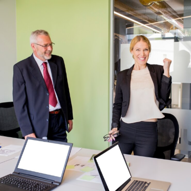 Dubai Company Setup - Two professionals standing near a table with two open laptops in an office setting.